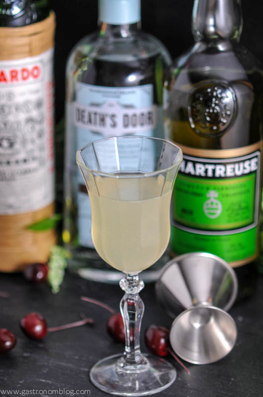 The Last Word Cocktail in a tall coupe glass with a jigger and bottles of gin, green chartreuse and maraschino liqueur. 