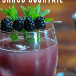 Purple cocktail in glass with blackberries and mint