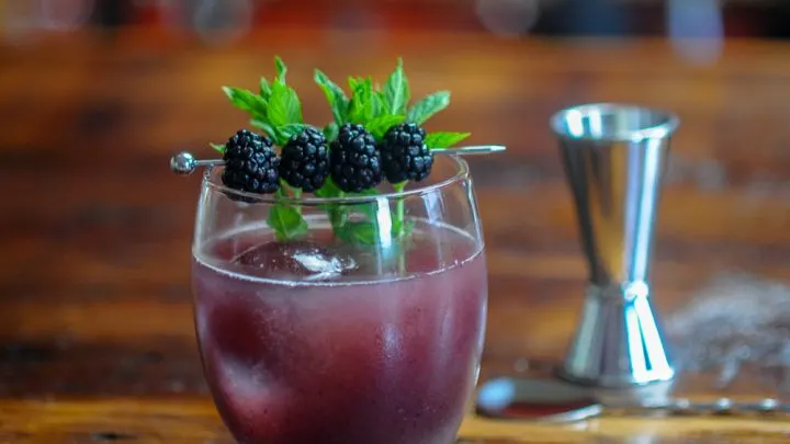 Honey Blackberry Whiskey Shrub Cocktail with clear ice. Blackberry and mint garnish.