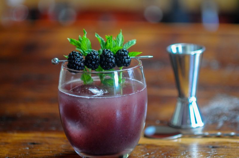 Blackberry Shrub Cocktail with clear ice. Blackberry and mint garnish. 
