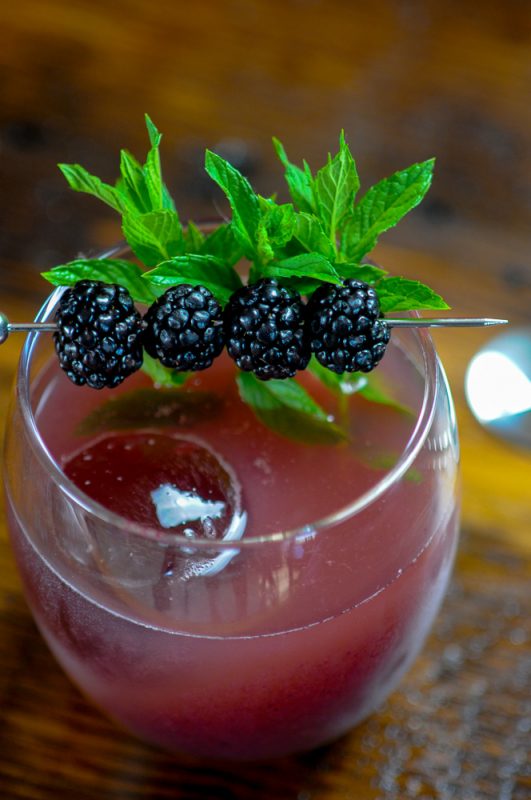 Purple Cocktail with clear ice. Blackberries and mint garnish.