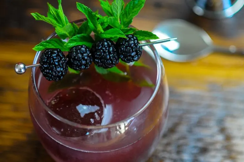 Shrub Cocktail in a glass with clear ice. Blackberries and mint garnish.
