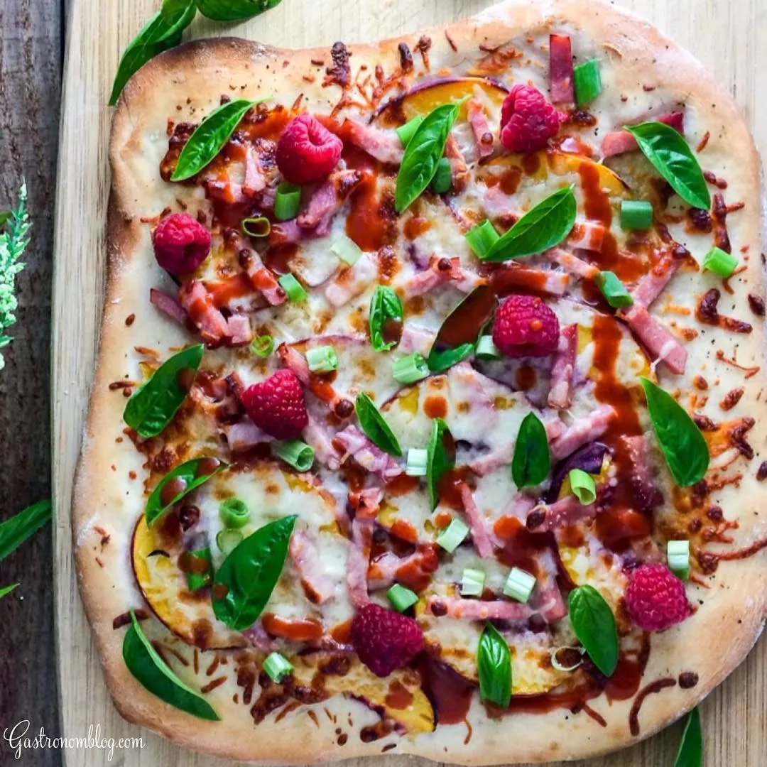 Top shot of pizza with hot sauce, ham, green onions, raspberries on it