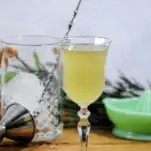 Green cocktail in coupe with mixing glass and juicer behind