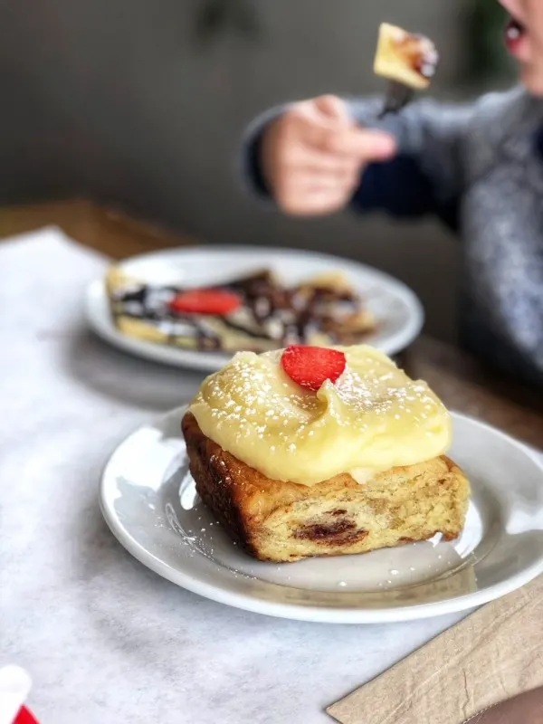 Cinnamon roll on white plate with frosting and raspberry on top at Overeasy Omaha