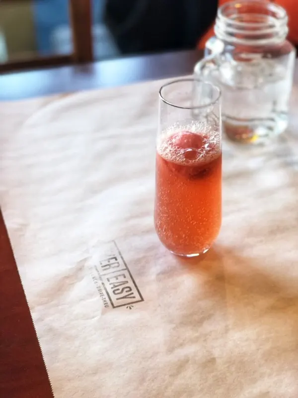 Pink champagne cocktail in tall flute on a table covered in brown paper