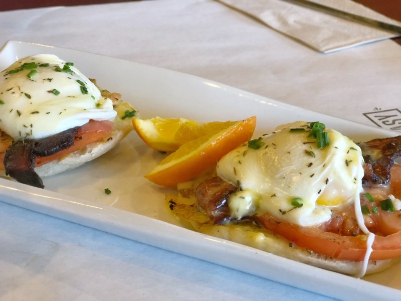 Eggs Benedict on toast on a white plate with orange slice in between