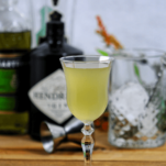 Green cocktail in coupe with bottles behind