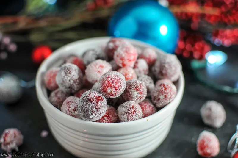 Sugared cranberries in a bowl with flowers and Christmas oranaments in the background