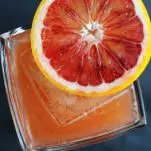 orange cocktail in rocks glass with orange slice on top