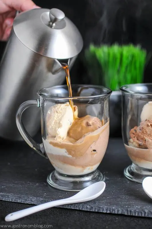 Coffee being poured from silver French press into glass mug with gelato, white ceramic spoon