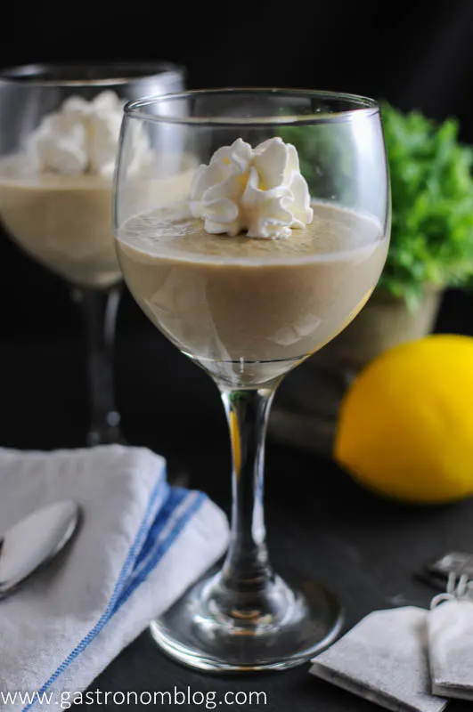 Earl Grey Pot de Creme in wine glass with whipped cream on top. Napkin, lemon and greenery behind wine glasses