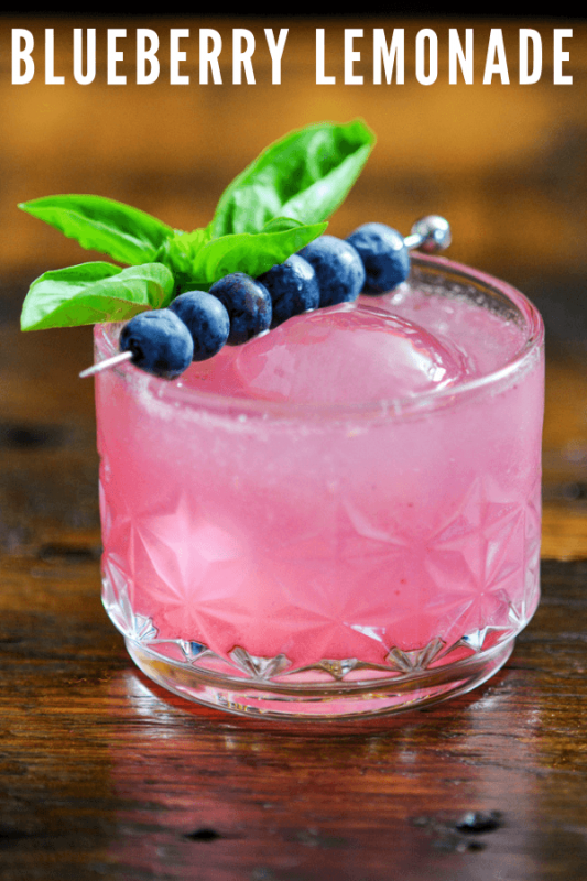 Pink cocktail with blueberries on cocktail pick and basil sprig
