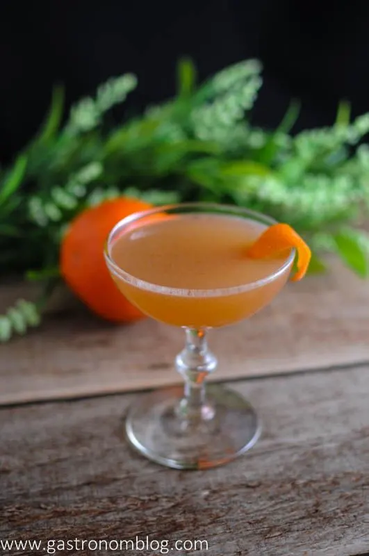 The Scofflaw Cocktail in a coupe on a wood board. Orange and leaves in background.
