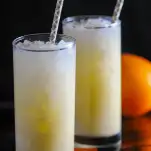 two orange cocktails in highball glasses, purple/white straws, orange behind