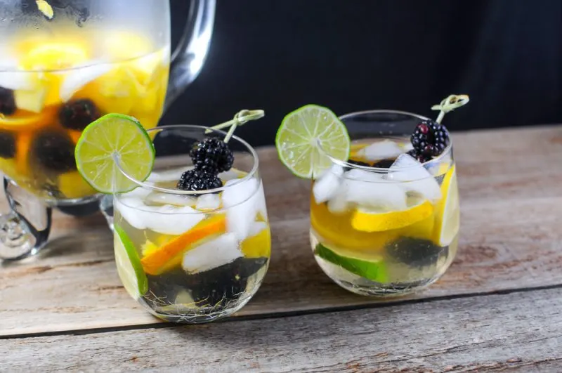 Sangria Punch with orange liqueur and a dry white wine. Limes, lemons, pineapple, oranges and blackberries from Gastronomblog. This Summer Punch recipe is sure to be great for a crowd. #wine #drink #lime #lemon #gastronomblog Sangria Blanca in glasses, pitcher in back