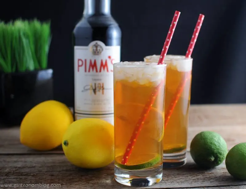 Pimm's Cup Cocktail in highballs with lemons and limes. Pimm's bottle and plant in background