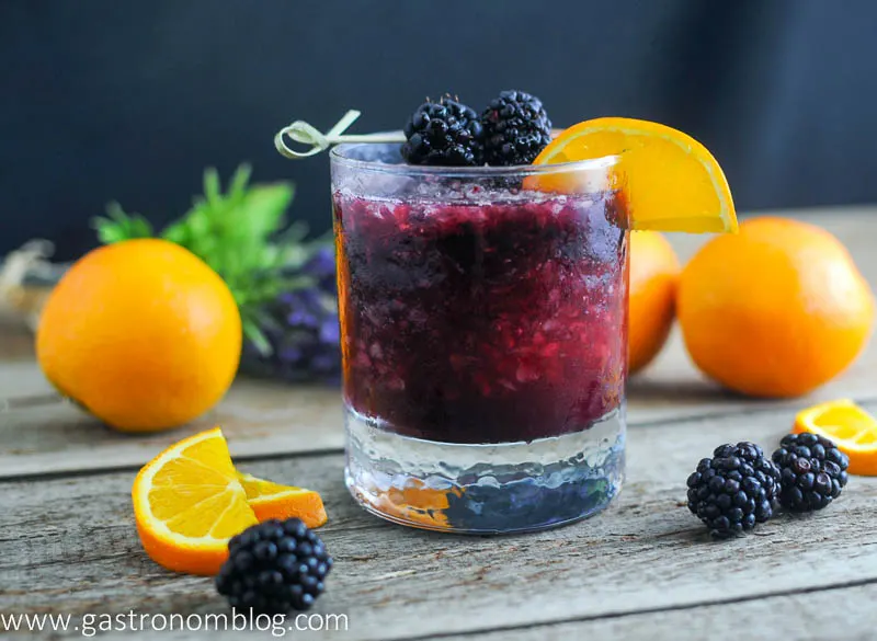 purple whiskey blackberry smash cocktail in rocks glass with oranges and blackberries