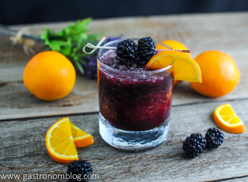 The Rambler Cocktail in a rocks glass with blackberries and oranges in the background