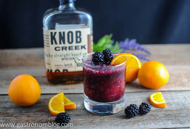 purple whiskey blackberry smash cocktail in rocks glass with oranges and blackberries