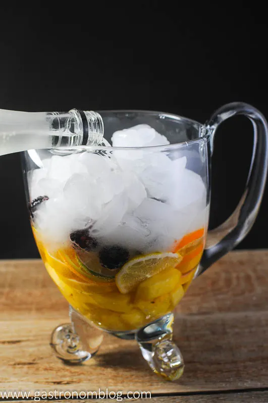Clear pitcher with limes, pineapple, lemons, oranges, blackberries topped with ice. Pouring in the wine.