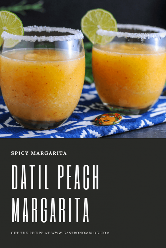 Datil Peach Frozen Margarita - 2 orange cocktails in glasses with salted rims and lime wheels. On a blue and white napkin
