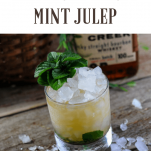 Mint Julep for the Kentucky Derby in rocks glass with crushed ice and mint. Basket and whiskey bottle in background.