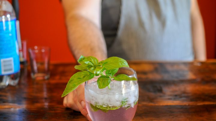 Rhubasil Cocktail in a glass with a basil bunch, man in apron