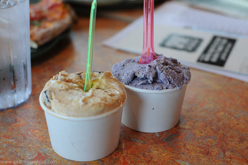 two white bowls with gelato in them. tan gelato with green spoon and purple gelato with pink spoon. Menu in background. 