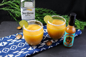 Datil Pepper Peach Frozen Margarita with hot sauce and tequila bottles on a blue and white napkin