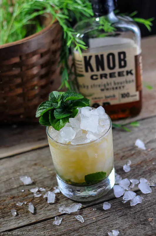 Mint Julep in a rocks glass with mint and heaped ice. Knob Creek bourbon bottle and basket in background