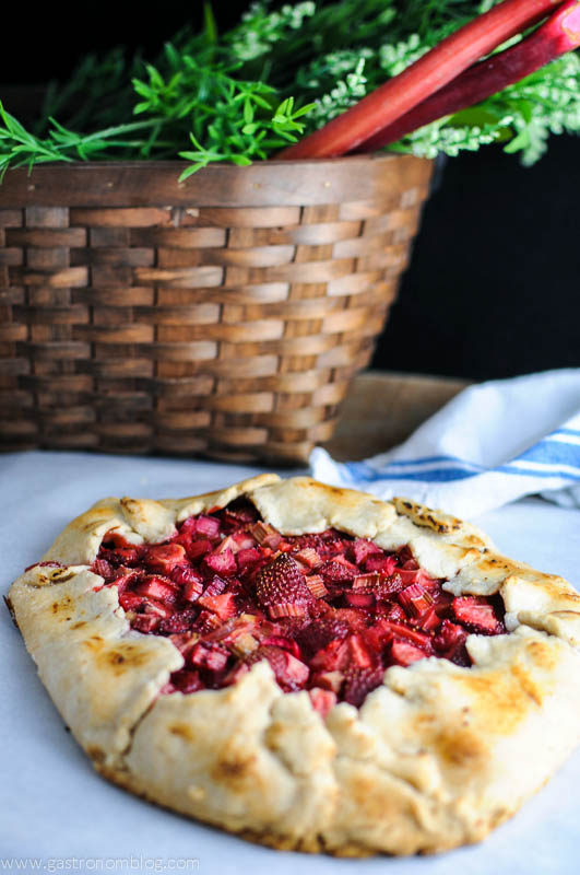 Tart with strawberries and rhubarb on parchment paper, basket with rhubarb behind