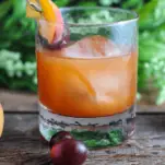 Peach Old Fashioned cocktail in rocks glass, peaches and cherries