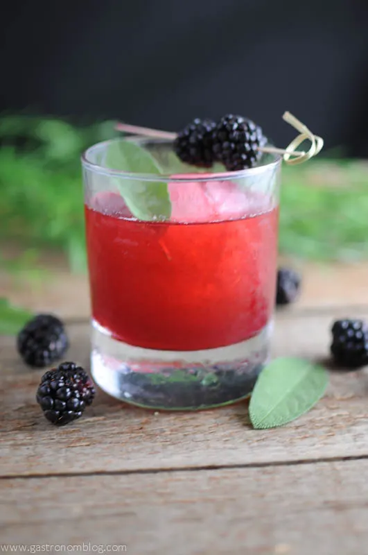 red blackberry sage cocktail in rocks glass with berries and sage leaves