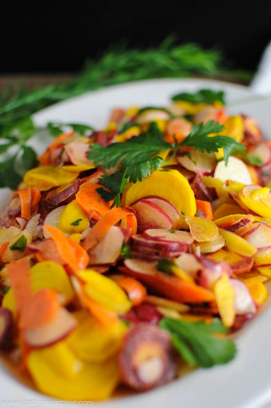Multicolored vegetables on a wihte plate with greenery in the background
