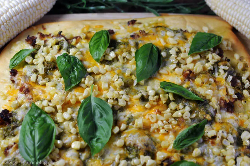 Sausage Corn and Pesto Pizza with ears of corn and basil on a cutting board