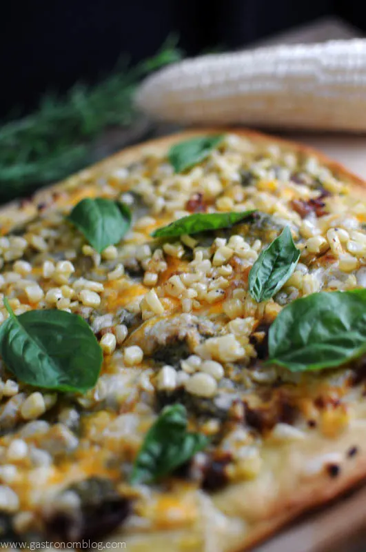 Pizza on cutting board with basil leaves, corn, sausage and cheese
