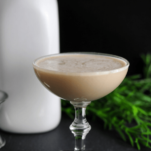 Creamy cocktail in coupe, white milk bottle and greens behind