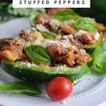 Stuffed Italian Peppers on white plate with tomatoes and basil leaves. Plate on white napkin, greenery in background.
