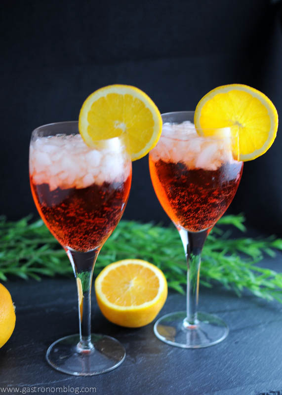 orange Aperol Spritz cocktails in wine glasses with orange slices. Cut orange and greenery in background