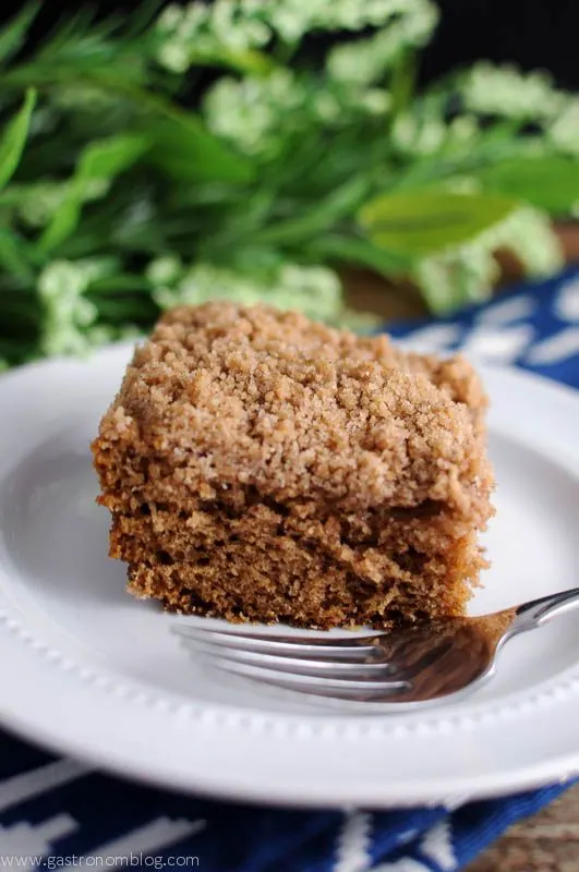 Streusel Topped Coffee Cake with fork on white plate. Blue and white napkin. Greenery behind