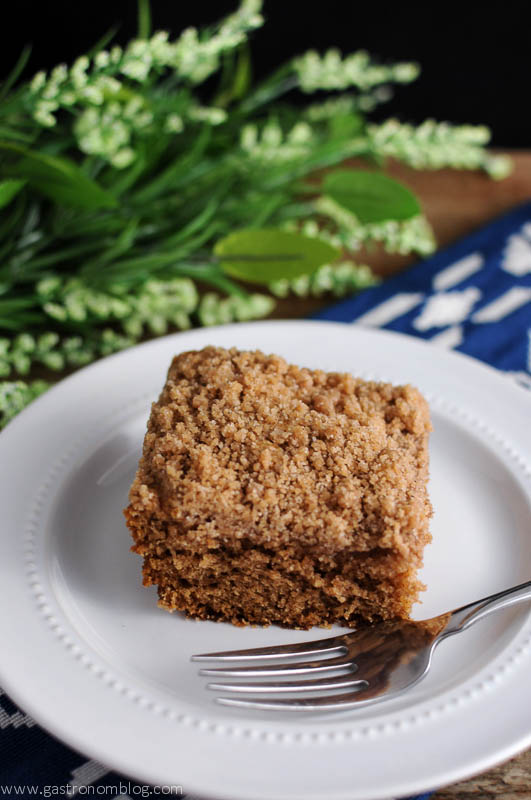 Coffee cake with fork on white plate. Blue and white napkin, Greenery behind
