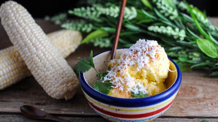 Mexican Street Corn Ice Cream - yellow ice cream in colorful striped bowl, ears of corn and flowers in background
