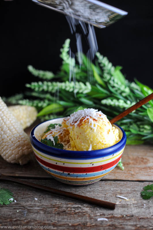 Yellow ice cream in colorful striped bowl. Wooden spoon, ears of corn and flowers in background
