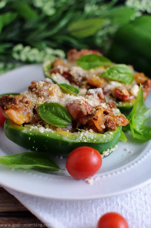 Green stuffed peppers with tomatoes on white plate, on white napkin with greenery behind