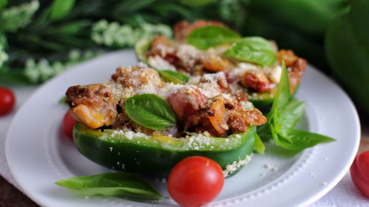 Green peppers stuffed with hamburger and tomatoes on white plate, on white napkin, with greenery behind