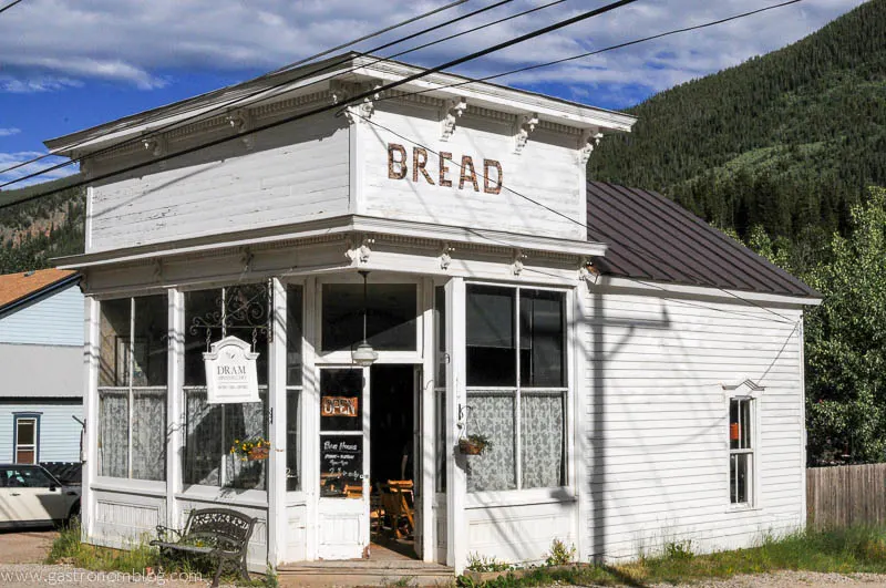 White building with bread written on side, blue side and mountain in background