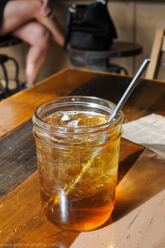 Brown cocktail in jar with ice and stainless steel straw on wooden table