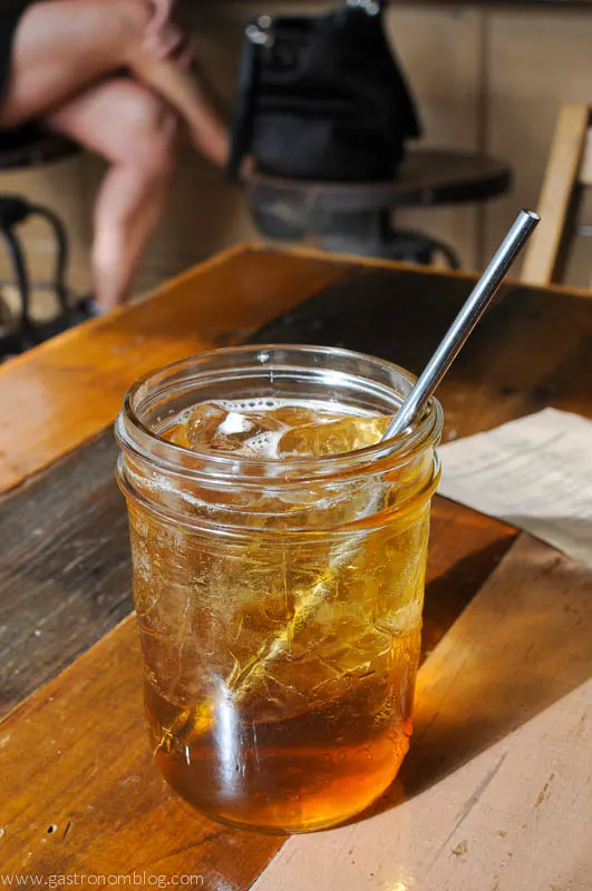 Brown cocktail in jar with ice and stainless steel straw on wooden table