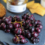 Purple grapes on slate board, jam with white spoon in back, crackers and cheese